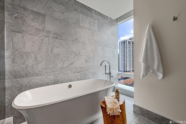 bathroom with tile patterned flooring, a tub to relax in, and tile walls