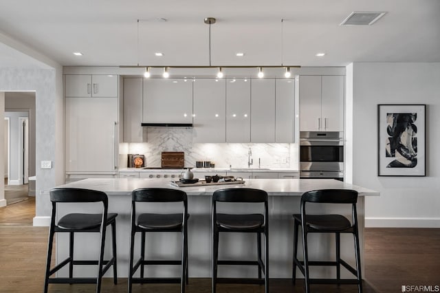 kitchen featuring a kitchen bar, dark wood-type flooring, sink, a center island, and hanging light fixtures