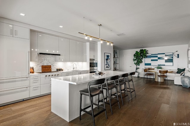 kitchen with a breakfast bar, wood-type flooring, stovetop, white cabinetry, and hanging light fixtures