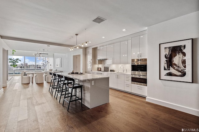 kitchen featuring a center island, light hardwood / wood-style flooring, pendant lighting, a breakfast bar, and white cabinets