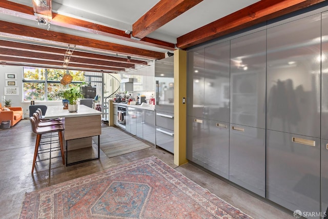 701 Pennsylvania Ave Unit 107, San Francisco, CA 94107 - kitchen featuring finished concrete flooring, modern cabinets, light countertops, beamed ceiling, and a breakfast bar