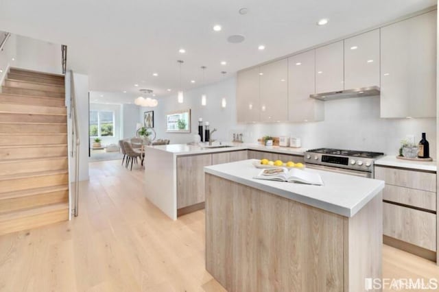 kitchen with white cabinets, hanging light fixtures, kitchen peninsula, stainless steel range with gas stovetop, and light hardwood / wood-style flooring