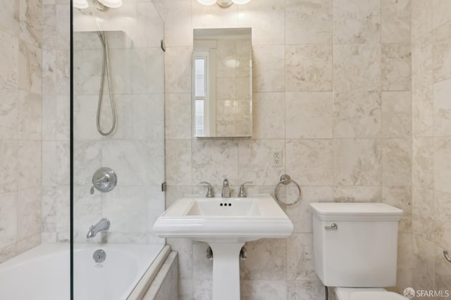 bathroom with tiled shower / bath, toilet, and tile walls