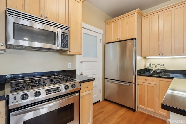 kitchen featuring light wood finished floors, light brown cabinetry, appliances with stainless steel finishes, and dark countertops