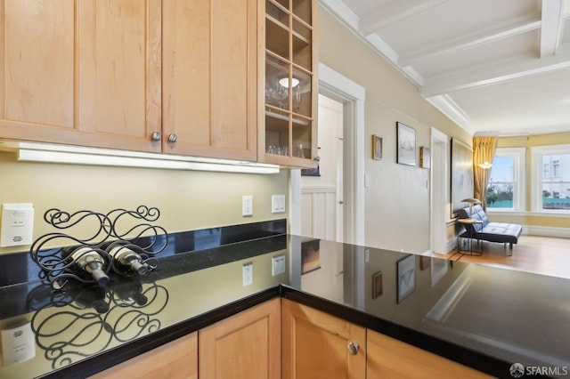 kitchen featuring dark countertops, glass insert cabinets, beam ceiling, and light brown cabinetry