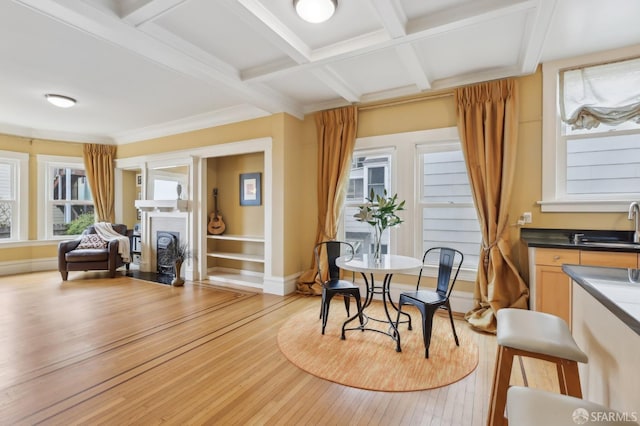 dining space featuring baseboards, coffered ceiling, light wood-style floors, a fireplace, and beam ceiling