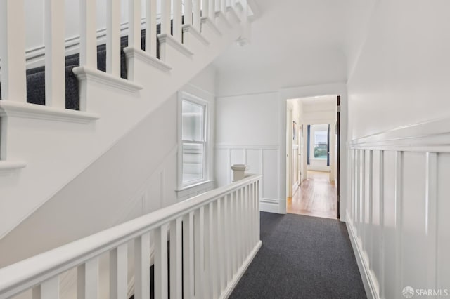 hallway featuring an upstairs landing, a decorative wall, and wainscoting