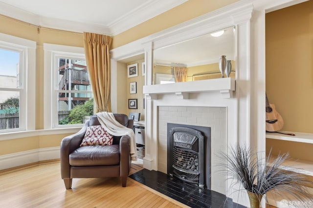 living area featuring baseboards, a fireplace, ornamental molding, and wood finished floors