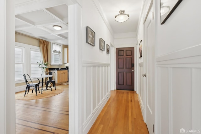 hallway featuring wainscoting, coffered ceiling, and light wood-style flooring