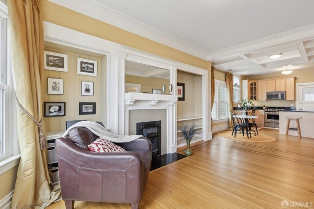 living room featuring coffered ceiling, light wood-style flooring, a fireplace with flush hearth, ornamental molding, and beamed ceiling