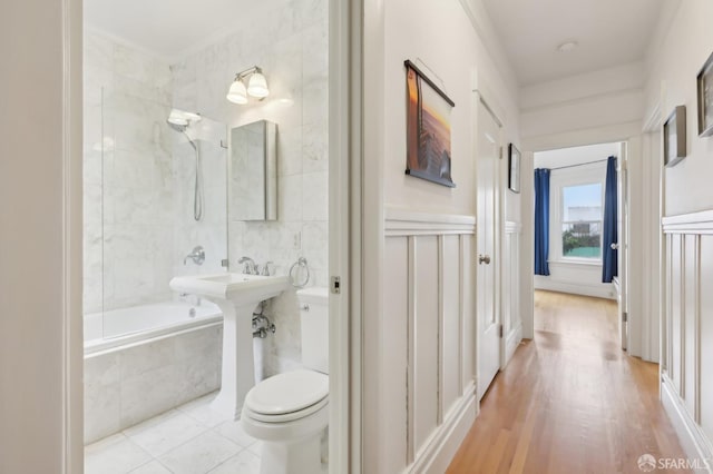 bathroom with tiled shower / bath, toilet, and tile walls