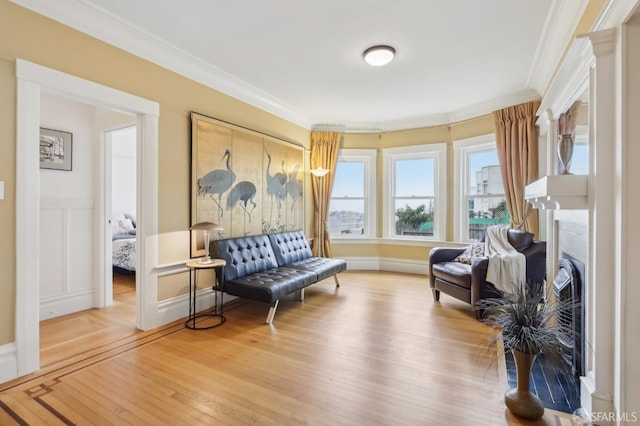 living area featuring a wainscoted wall, light wood finished floors, a fireplace, and crown molding