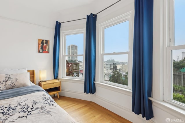 bedroom with baseboards, a city view, and light wood-style floors