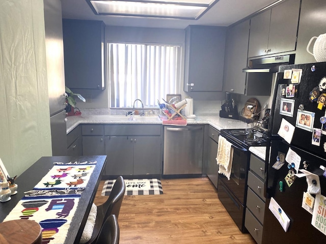 kitchen featuring light wood-style flooring, under cabinet range hood, light countertops, black appliances, and a sink