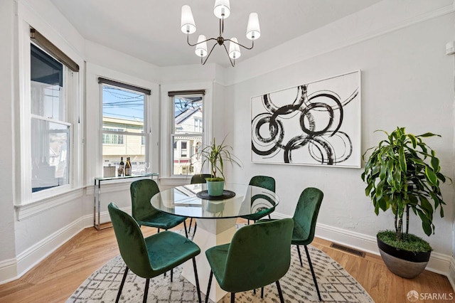 dining area with light wood-type flooring, an inviting chandelier, visible vents, and baseboards