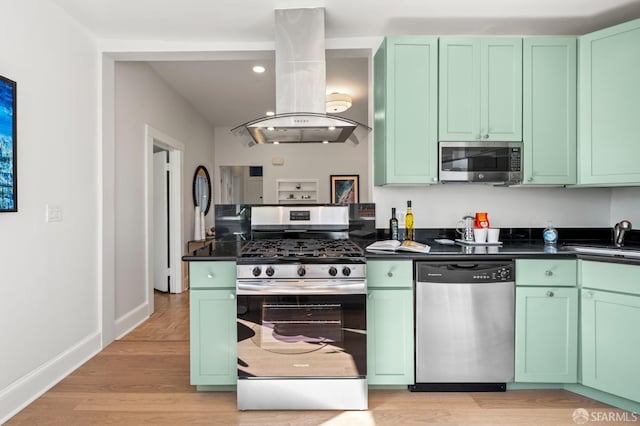 kitchen with green cabinetry, dark countertops, appliances with stainless steel finishes, island exhaust hood, and a sink