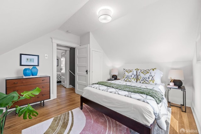 bedroom featuring light wood-type flooring, lofted ceiling, and baseboards