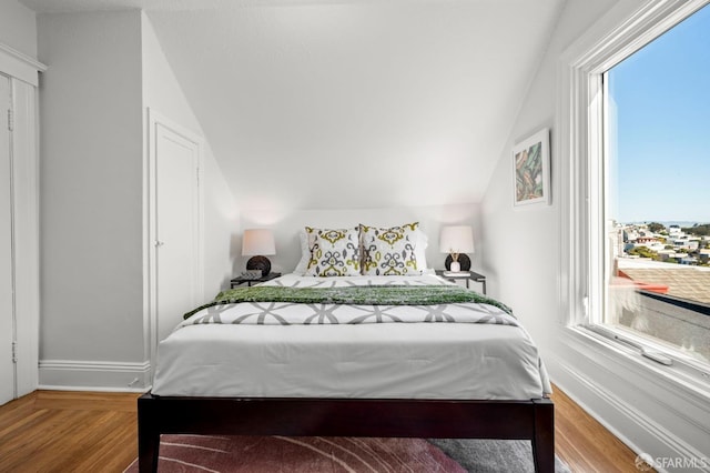 bedroom with vaulted ceiling, wood finished floors, and baseboards