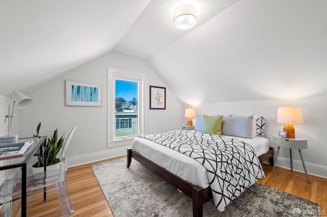 bedroom featuring lofted ceiling, baseboards, and wood finished floors