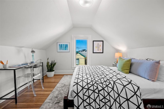 bedroom with baseboards, vaulted ceiling, and wood finished floors