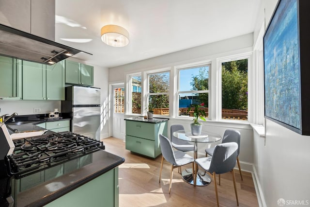 kitchen featuring ventilation hood, dark countertops, freestanding refrigerator, and green cabinetry