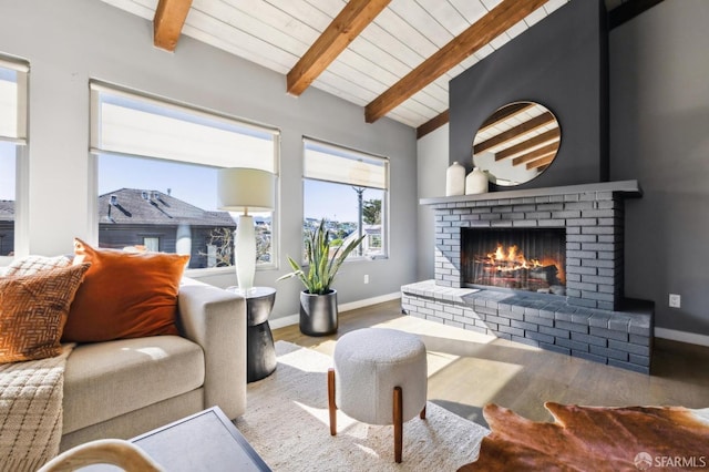 living area with lofted ceiling with beams, a brick fireplace, baseboards, and wood finished floors