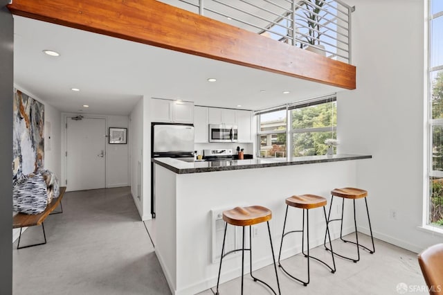 kitchen featuring appliances with stainless steel finishes, beamed ceiling, white cabinetry, dark stone counters, and kitchen peninsula