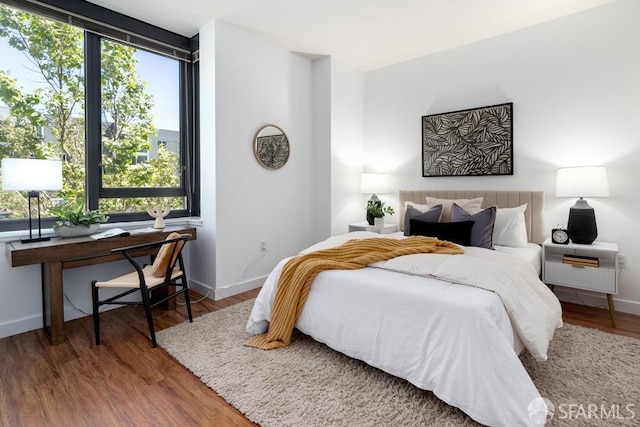 bedroom with multiple windows, baseboards, and wood finished floors