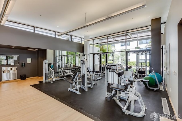 gym with a towering ceiling, floor to ceiling windows, and wood finished floors