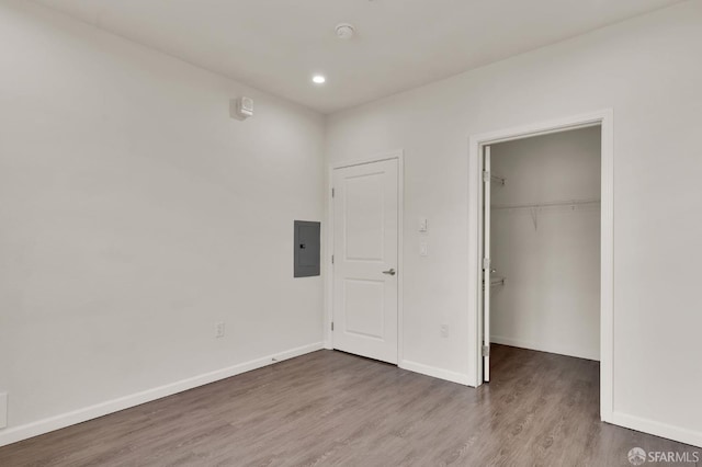 unfurnished bedroom with electric panel, a spacious closet, a closet, and dark wood-type flooring