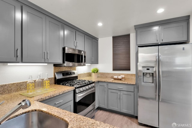 kitchen featuring light stone countertops, gray cabinets, stainless steel appliances, and light hardwood / wood-style flooring