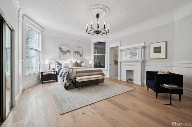 bedroom with a textured ceiling, an inviting chandelier, light hardwood / wood-style flooring, and multiple windows