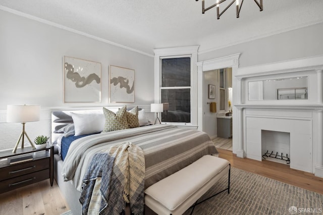 bedroom with ensuite bathroom, an inviting chandelier, crown molding, light wood-type flooring, and a textured ceiling