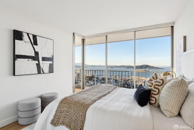 bedroom with a water view, wood finished floors, access to exterior, baseboards, and floor to ceiling windows