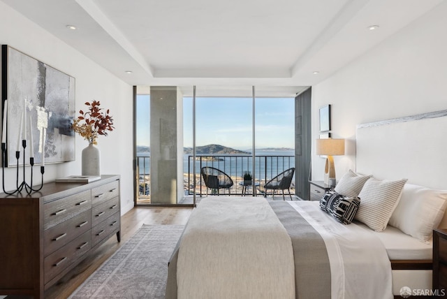 bedroom with wood finished floors, access to outside, a tray ceiling, floor to ceiling windows, and recessed lighting