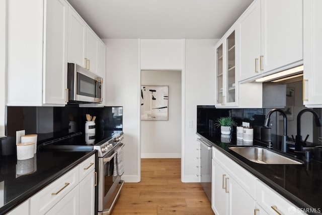 kitchen with dark countertops, appliances with stainless steel finishes, a sink, white cabinetry, and backsplash