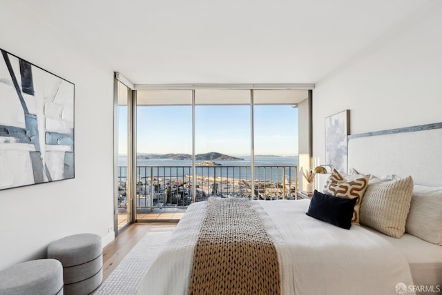 bedroom with expansive windows, access to outside, a water view, and wood finished floors