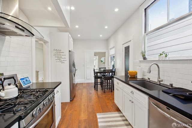 kitchen with appliances with stainless steel finishes, dark hardwood / wood-style floors, white cabinets, wall chimney range hood, and sink