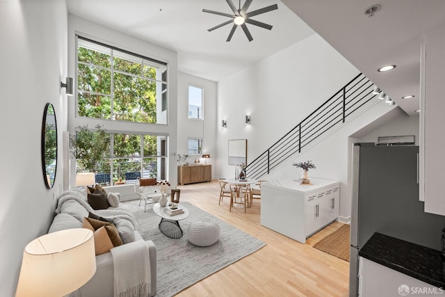 living room featuring ceiling fan, a healthy amount of sunlight, light hardwood / wood-style flooring, and a high ceiling