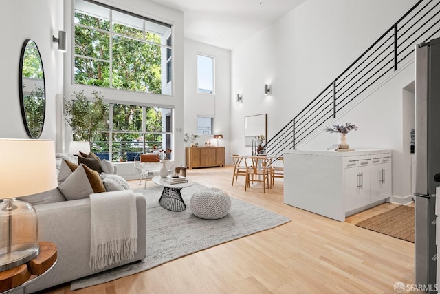 living room with a healthy amount of sunlight, light hardwood / wood-style flooring, and a towering ceiling