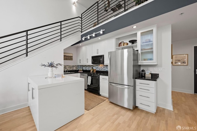 kitchen featuring black appliances, light hardwood / wood-style floors, white cabinets, and a towering ceiling