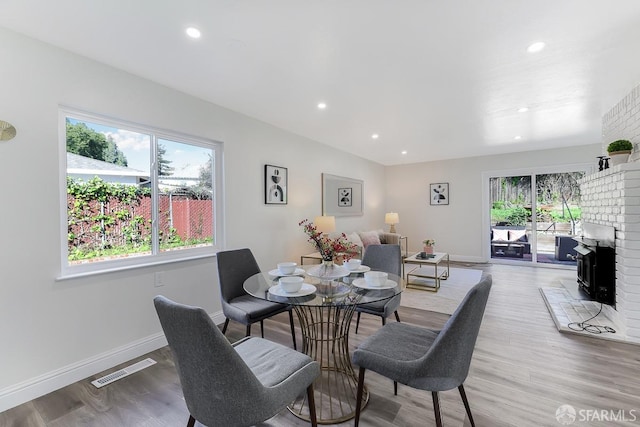 dining space with plenty of natural light, wood-type flooring, and a brick fireplace