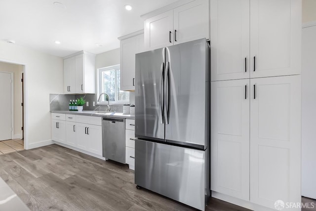 kitchen featuring decorative backsplash, stainless steel appliances, sink, wood-type flooring, and white cabinets