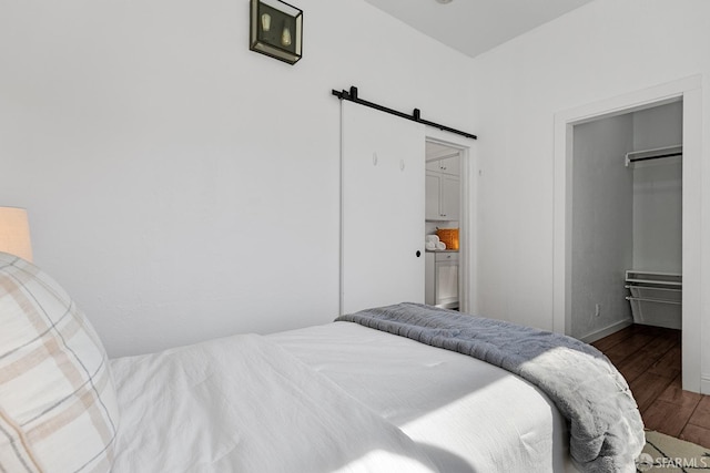 bedroom with a barn door, a walk in closet, and wood finished floors