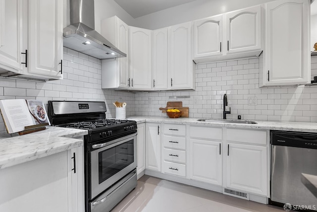 kitchen featuring visible vents, a sink, appliances with stainless steel finishes, wall chimney exhaust hood, and white cabinets