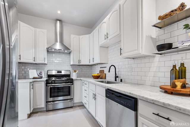 kitchen with white cabinets, appliances with stainless steel finishes, wall chimney range hood, and a sink