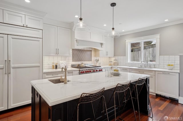 kitchen featuring sink, light stone counters, a center island with sink, stainless steel gas stovetop, and white cabinets