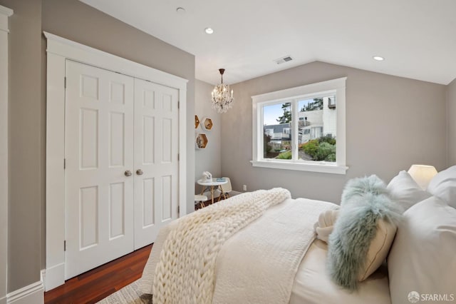 bedroom with lofted ceiling, a notable chandelier, dark wood-type flooring, and a closet