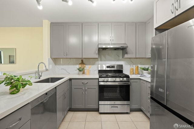 kitchen with stainless steel appliances, under cabinet range hood, a sink, and gray cabinets