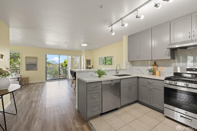 kitchen featuring a sink, gray cabinets, stainless steel appliances, a peninsula, and under cabinet range hood